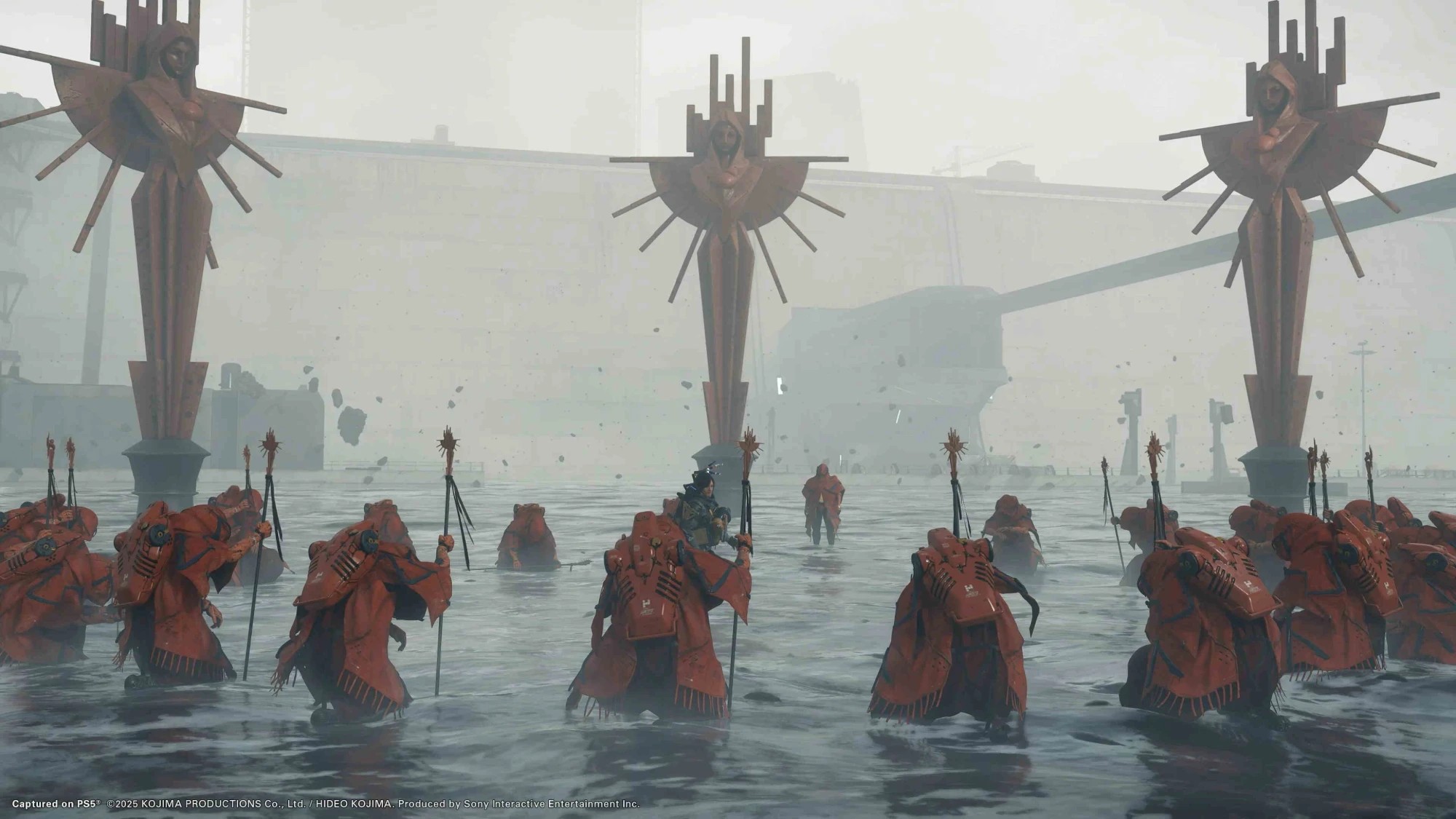 A scene from Death Stranding 2: red-robed figures wading through water beneath three tall statues