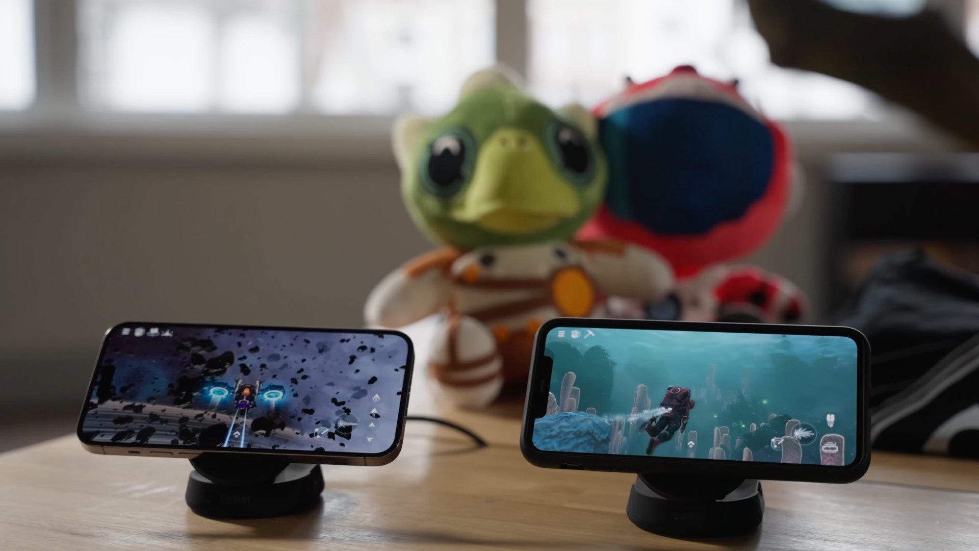 Hai chiếc iPhone đặt ngang trên bàn chạy No Man's Sky, phía sau là hai thú nhồi bông