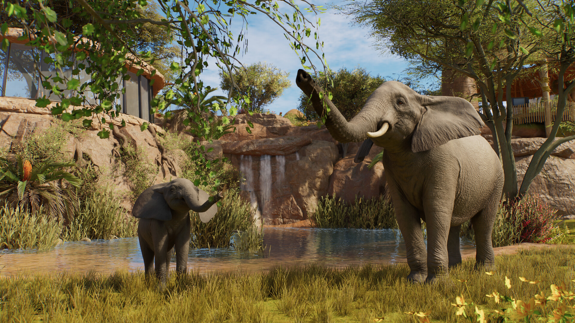 An adult elephant and a calf stand beside a pool, with a small waterfall behind their habitat in Planet Zoo 2.