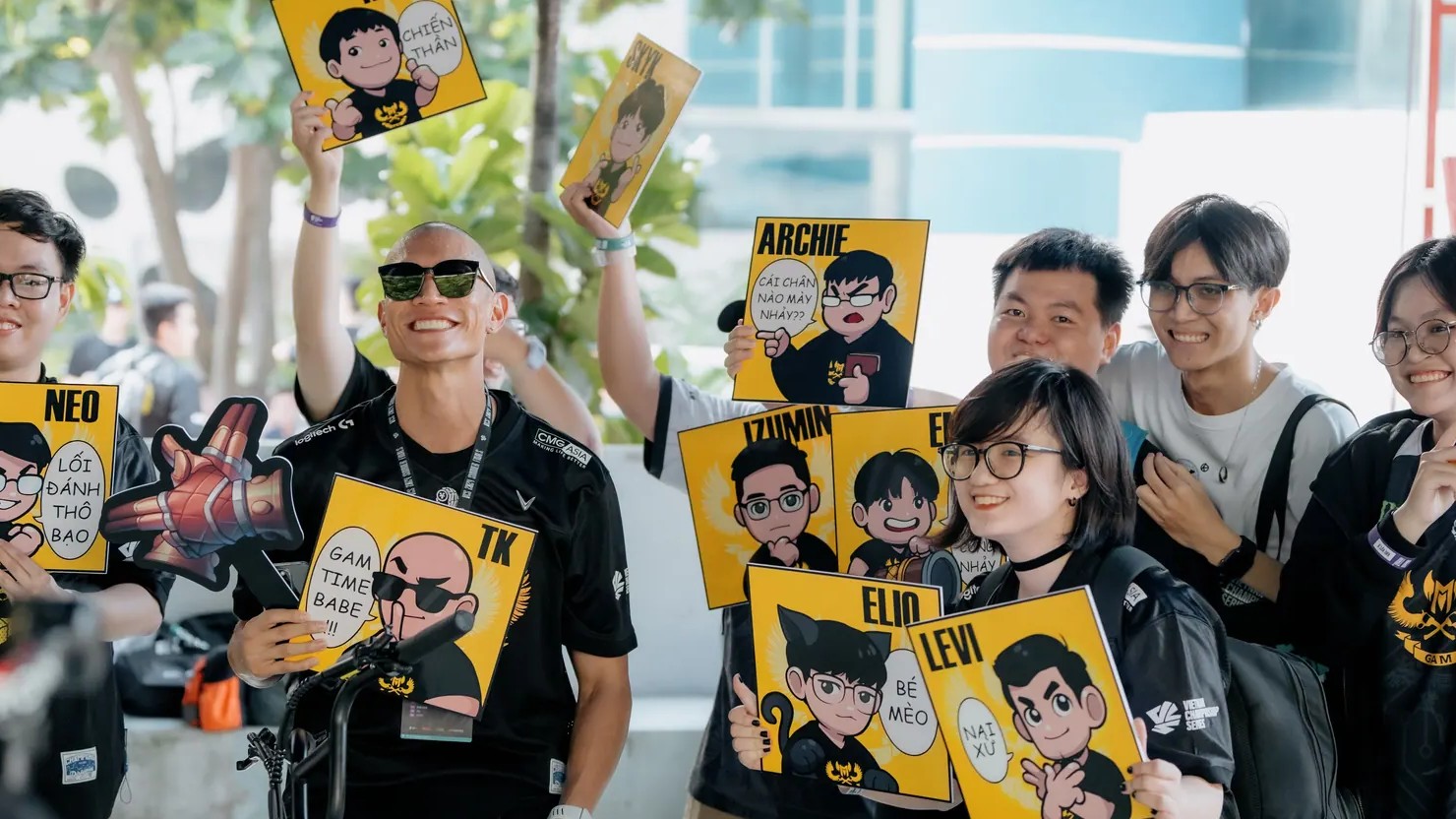 GAM Esports fans holding up cheer boards with cartoon portraits of players and club leaders, with a smiling man in sunglasses in the middle