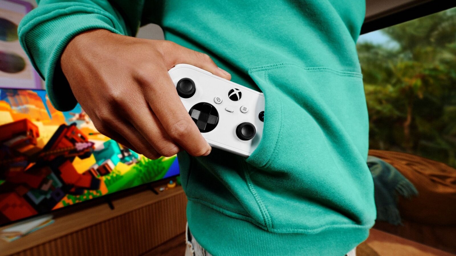 Một bàn tay rút Xbox Nano Controller màu trắng khỏi túi áo hoodie xanh